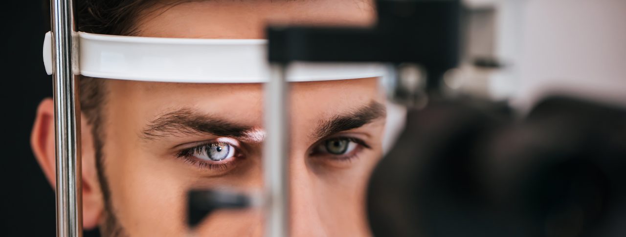 Close up image of a man having an eye examination. His chin is resting on the slit lamp, and a light is shining on his eye.