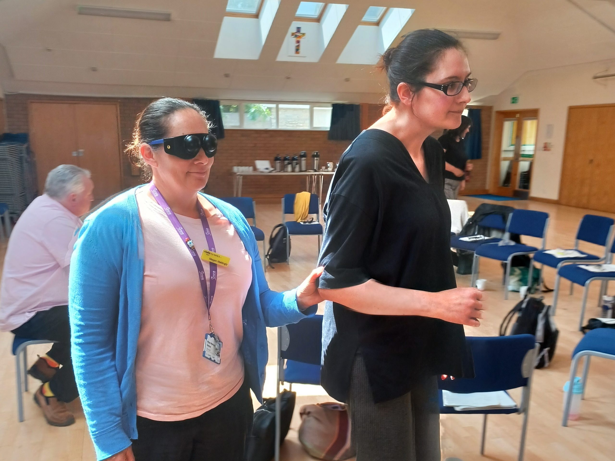 Two members of staff are participating in the sighted guide training. One member of staff is leading the other.
