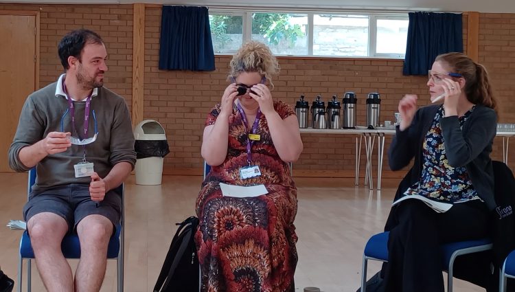 Three members from the Sirona Diabetes and Nutrition Services team are sat down, trying on simulation specs. They are talking to each other as they try them on.