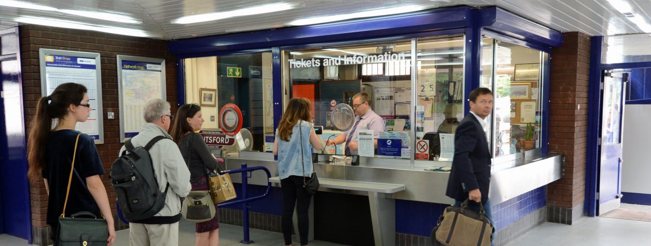 Several people queueing up at a ticket office in a train station.