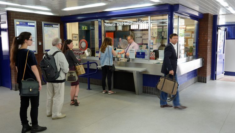 Several people queueing up at a ticket office in a train station.