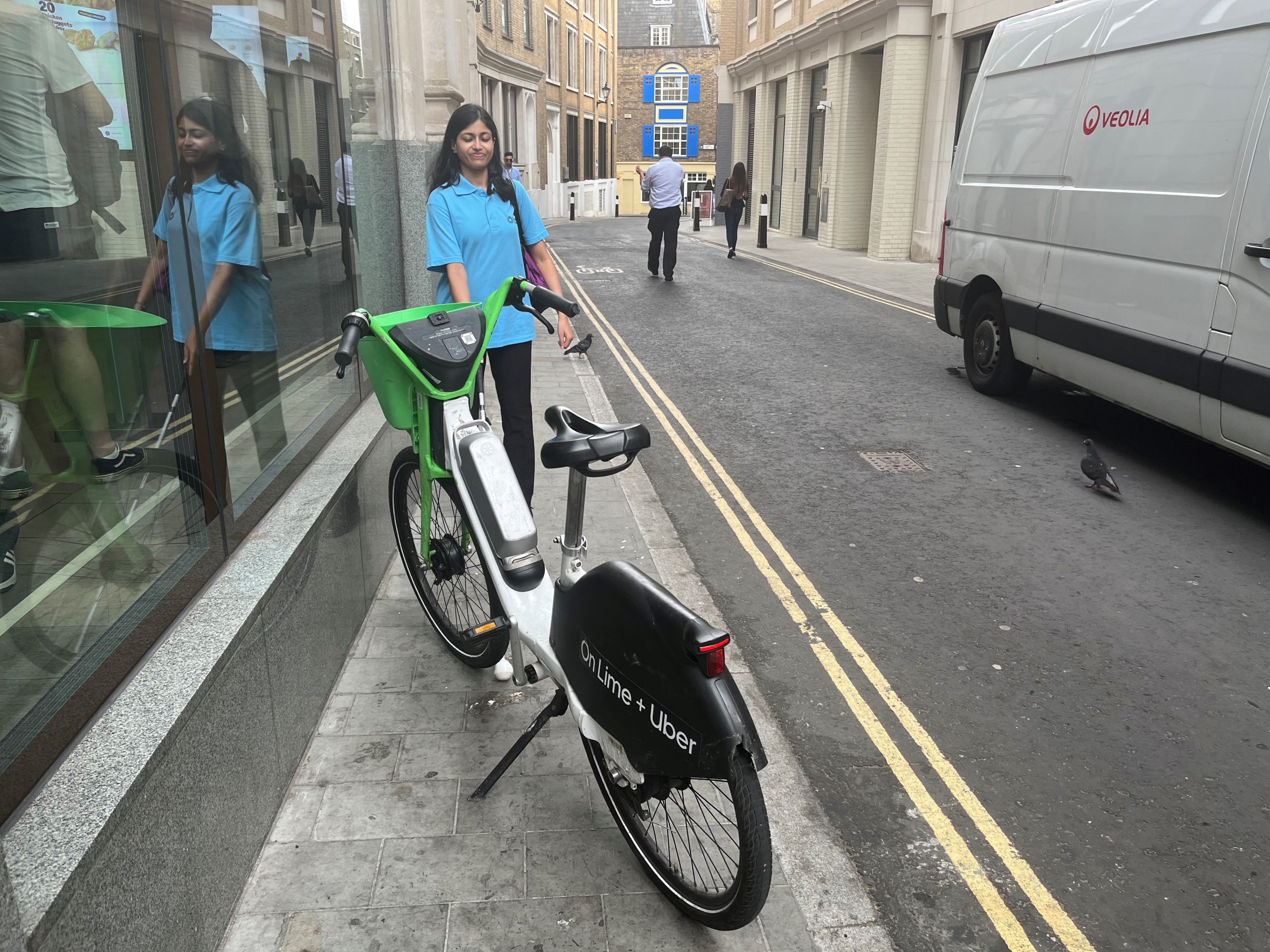 Vidya Nathan, London SLC member, is walking down a narrow pavement next to a road. Using her long cane, she encounters a Lime Bike parked across the pavement which prevents her from passing.