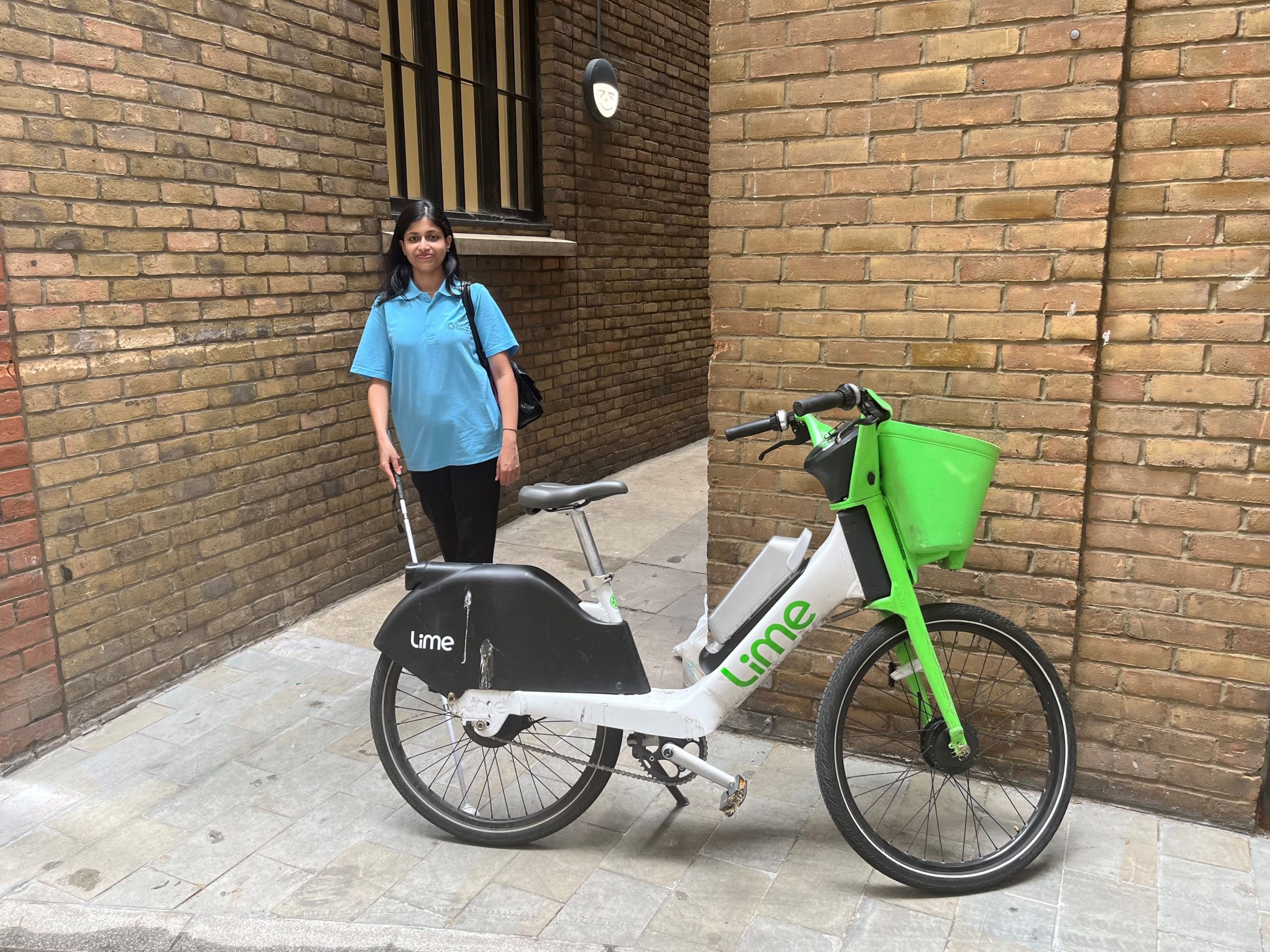 Vidya Nathan, London SLC member, is walking down an alley using her long cane. The path is obstructed by a Lime bike, which has been parked across the entrance.