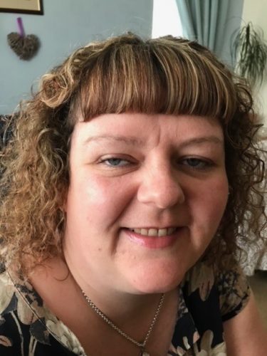A headshot of Greater Manchester SLC member, Rachael Foley. She has brown, curly, shoulder length hair. Rachel is looking at the camera, smiling.