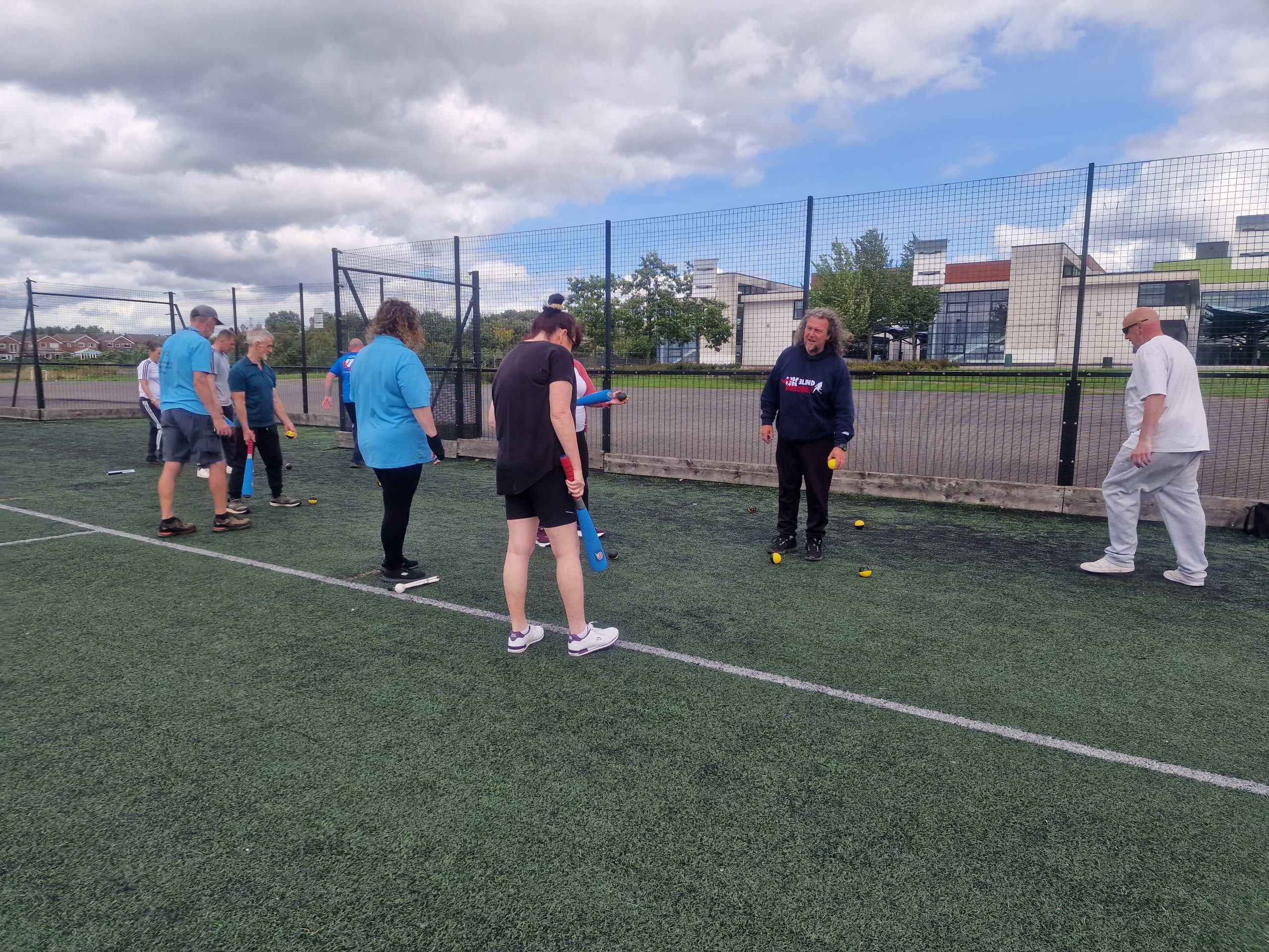 A group of blind and partially sighted attendees are practising baseball techniques outside.