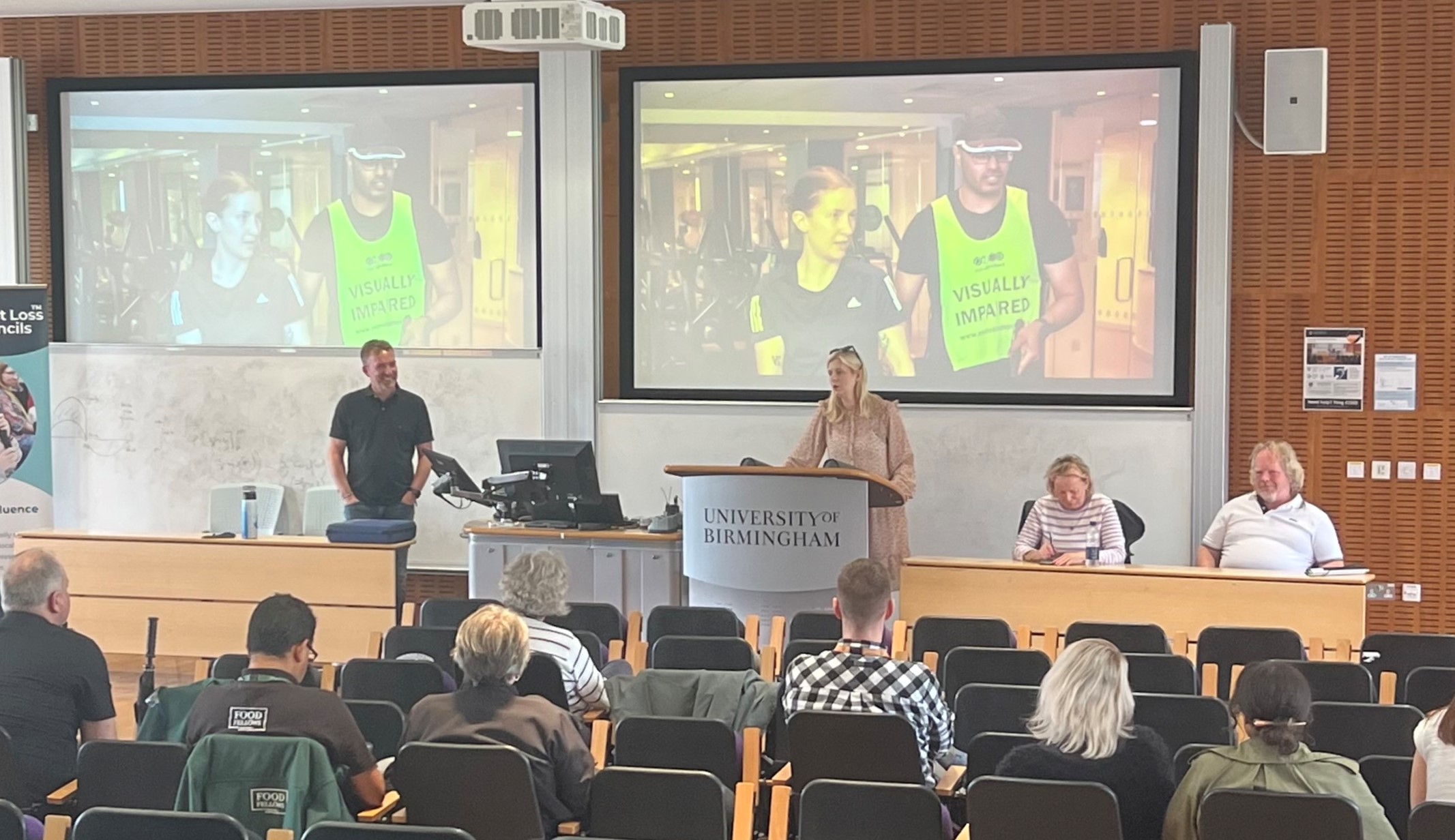 Louise Connop, Senior Engagement Manager for Central England is with Martin Symcox, Head of sport and Leisure at TPT, and SLC members. They are on stage, presenting to university staff.