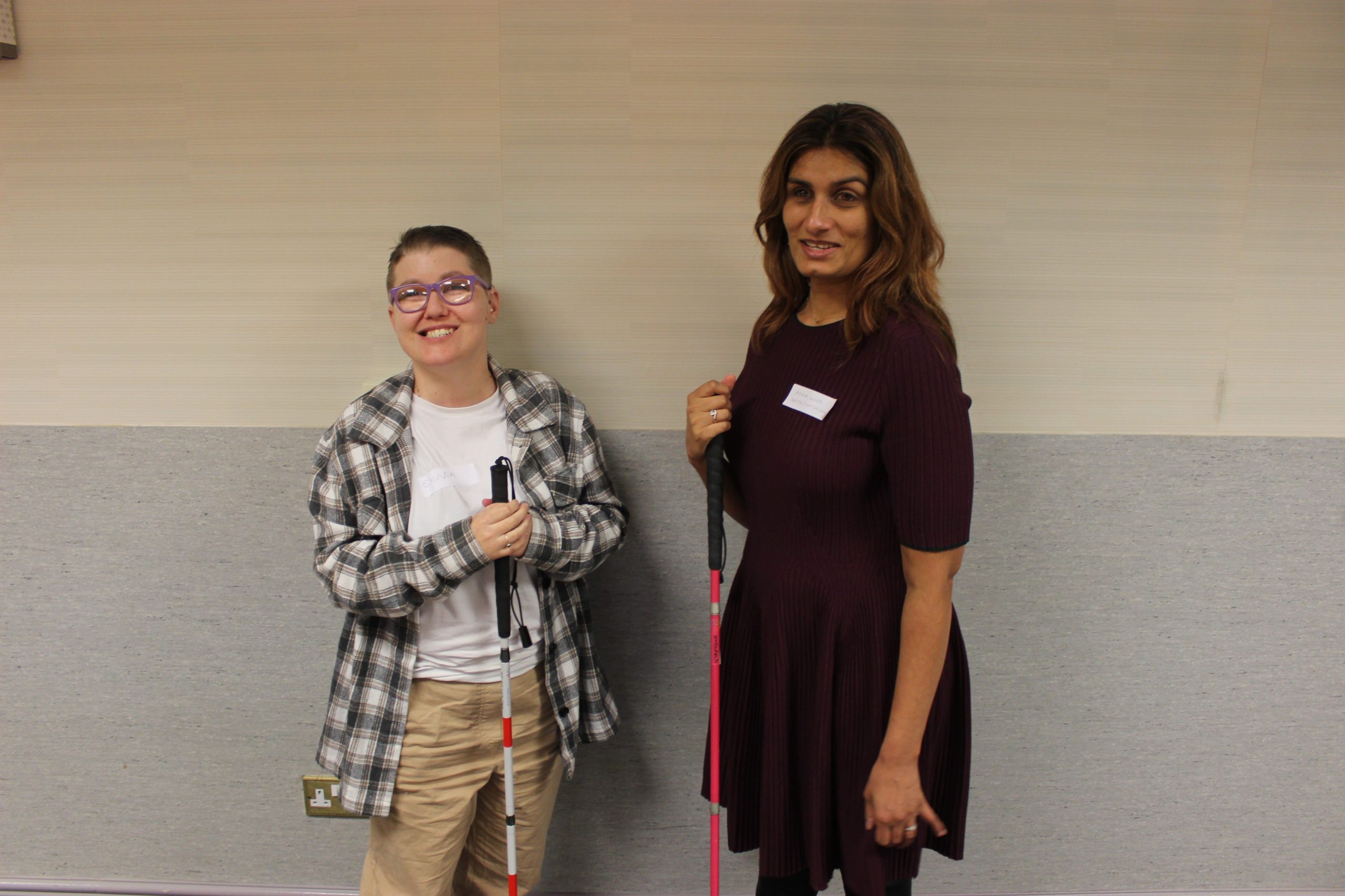 Emma Blackmore and Anela Wood pictured together at an NBT volunteer event where they spoke about their work with the trust. They are both looking and smiling at the camera, and holding their long canes.