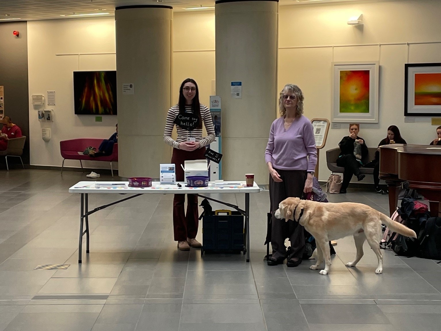 Rosie, NBT staff member, pictured with Heather Armstrong, West of England SLC member during an AIS roadshow. They are pictured with Heather's guide dog at their information stall.