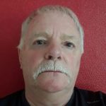 Headshot of Geoff Pickance, Nottinghamshire SLC member. He is standing against a red wall, looking at the camera.