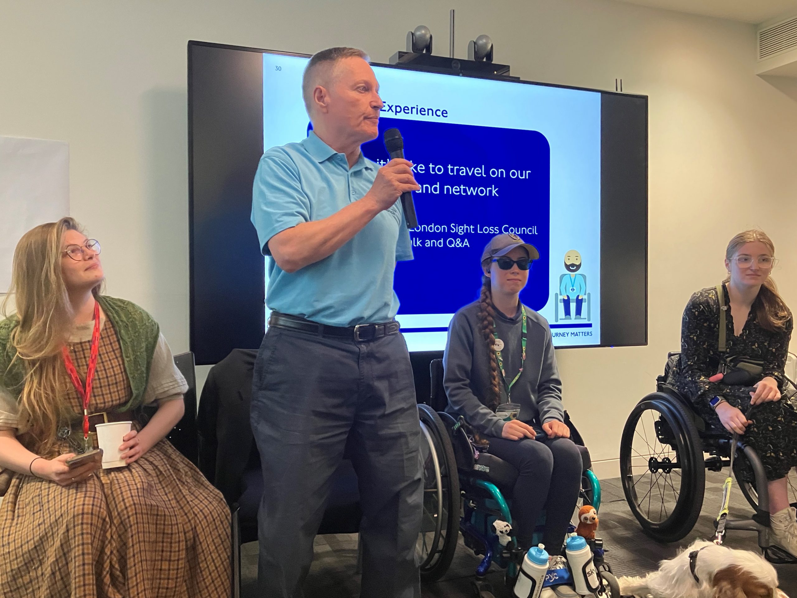 South West London SLC member, Harry, presenting to the Fleet Renewals team. He is standing up in front of an overhead projector screen, speaking into a microphone.