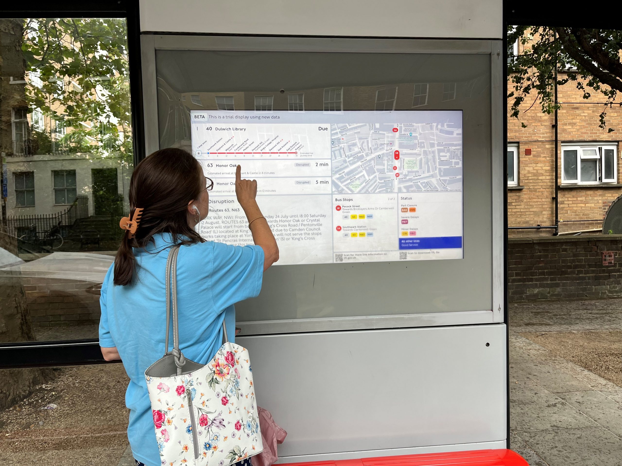 South west London SLC member, Vicky, standing at a bus stop, with a trial digital display. Vicky is standing with her back to the camera, pointing at the display.