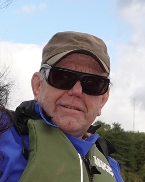 Photo of Micahel Parkinson, Lancashire SLC member. Michael is outside, wearing a khaki life jacket over a blue coat. He is wearing a khaki cap and black sunglasses.