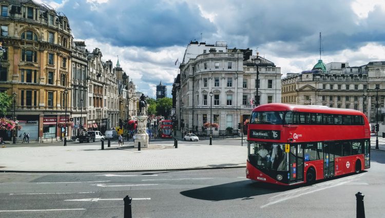 A red London bus, shown going round a roundabout at Trafalgar Square, London.
