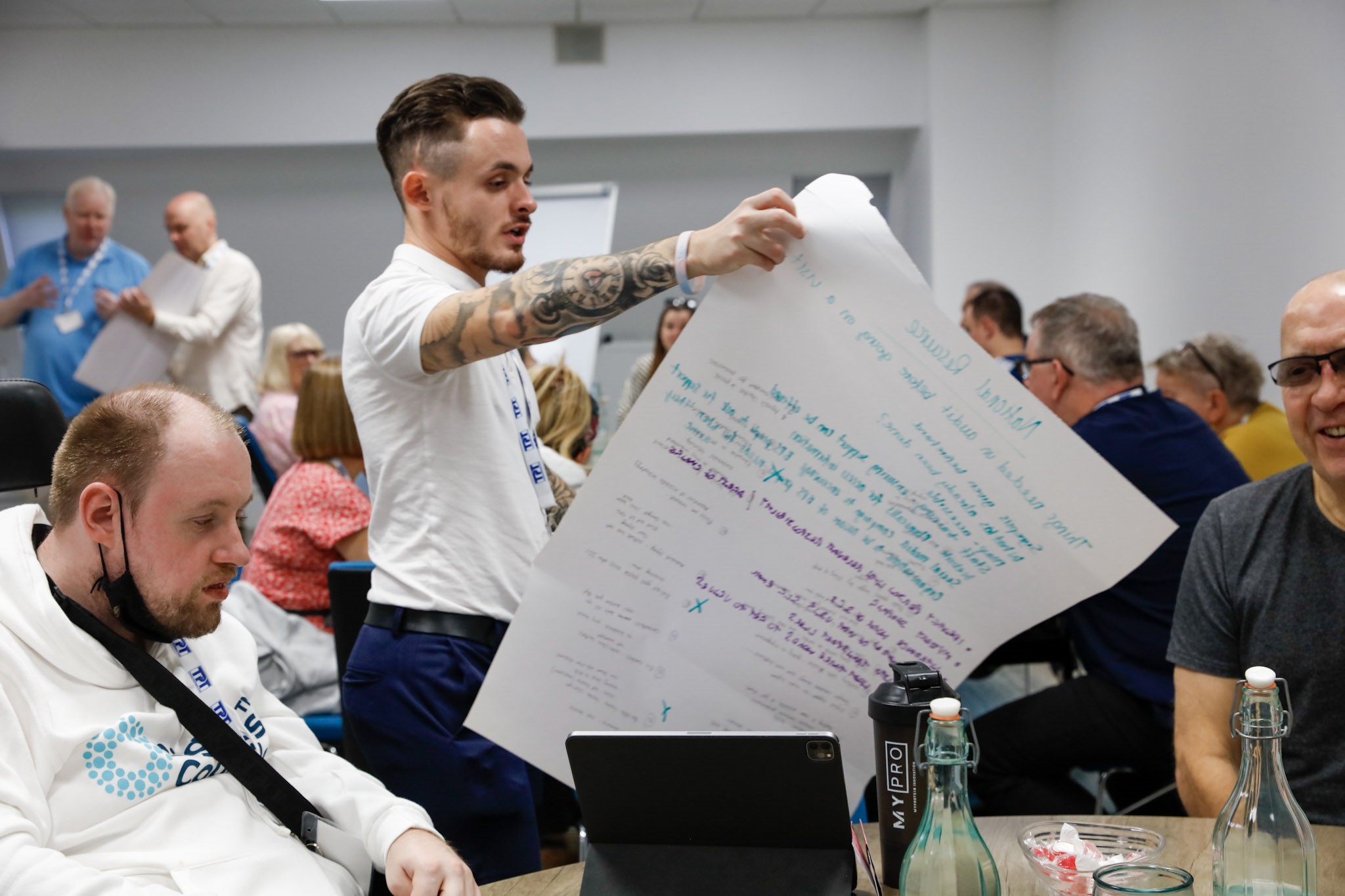 David Parfett, SLC Coordinator for the North West, reading from a large sheet of paper with notes on it at a table of delegates during a session at the SLC conference.