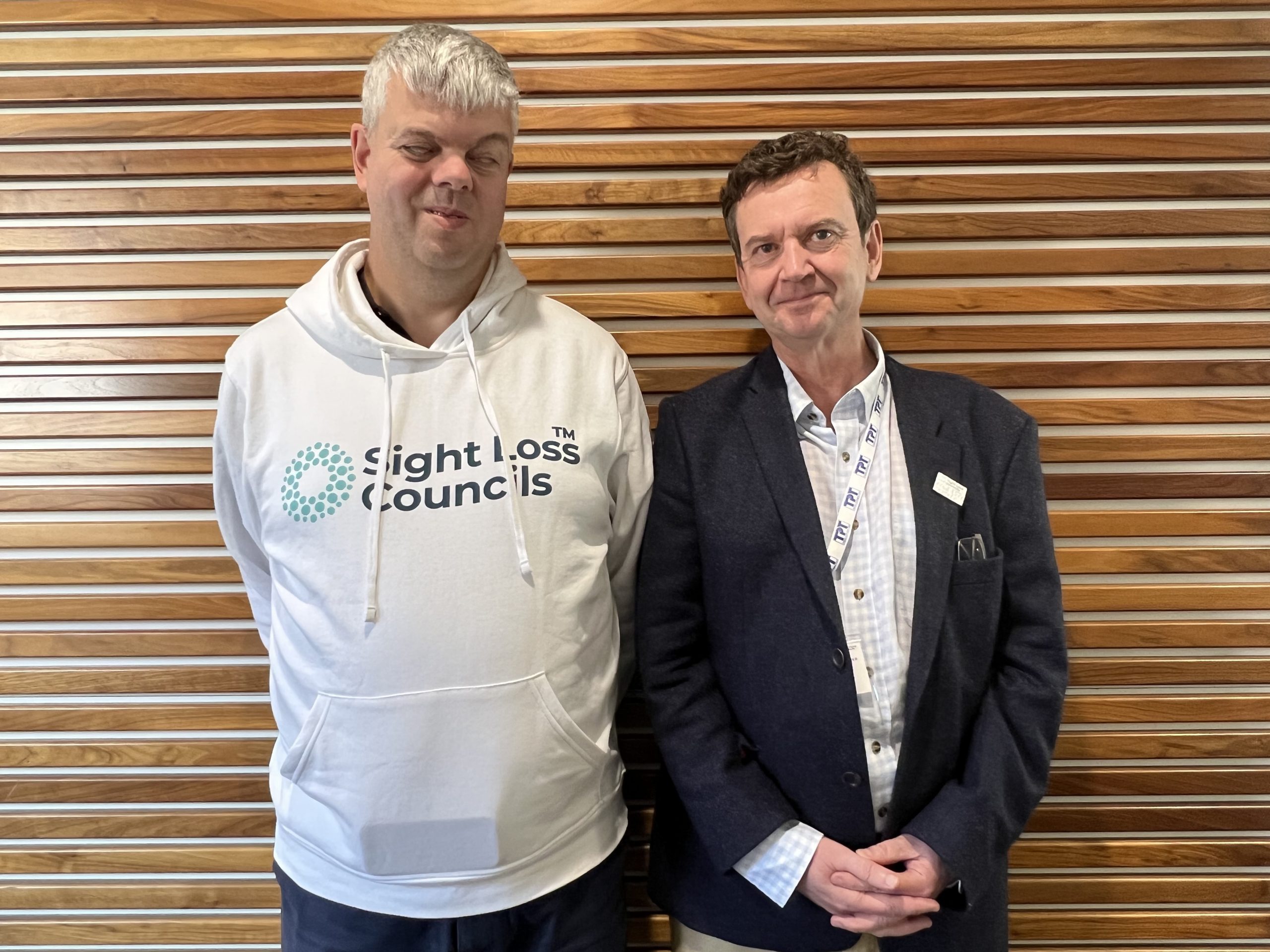 David Clarke OBE, and Charles Colquhoun, CEO of Thomas Pocklington Trust. They are stood together against a wood panelled wall, smiling at the camera. David is wearing a white SLC hoodie.