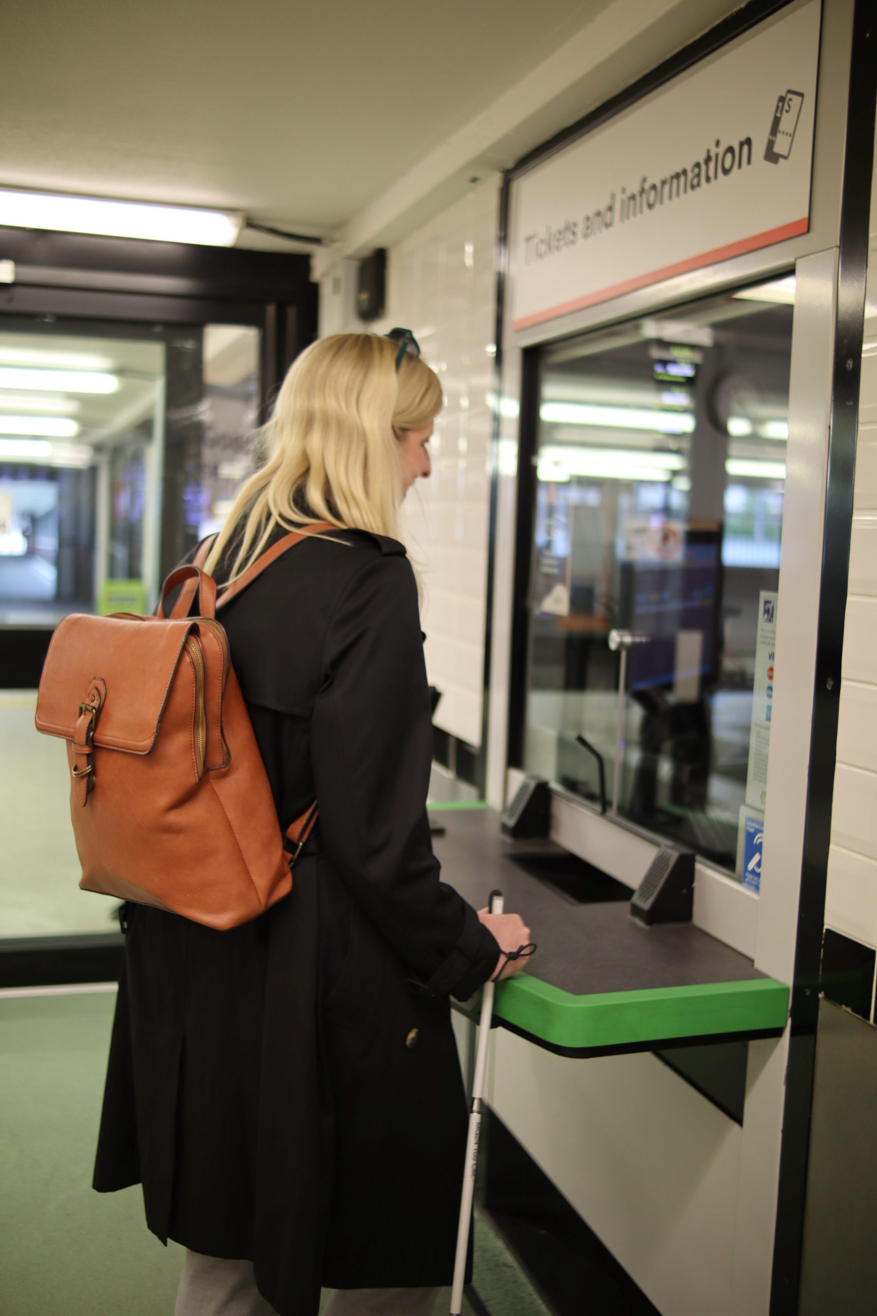 Louise Connop, Senior Engagement Manager for Sight Loss Councils, purchasing a ticket from a ticket office counter. She is holding her long cane.