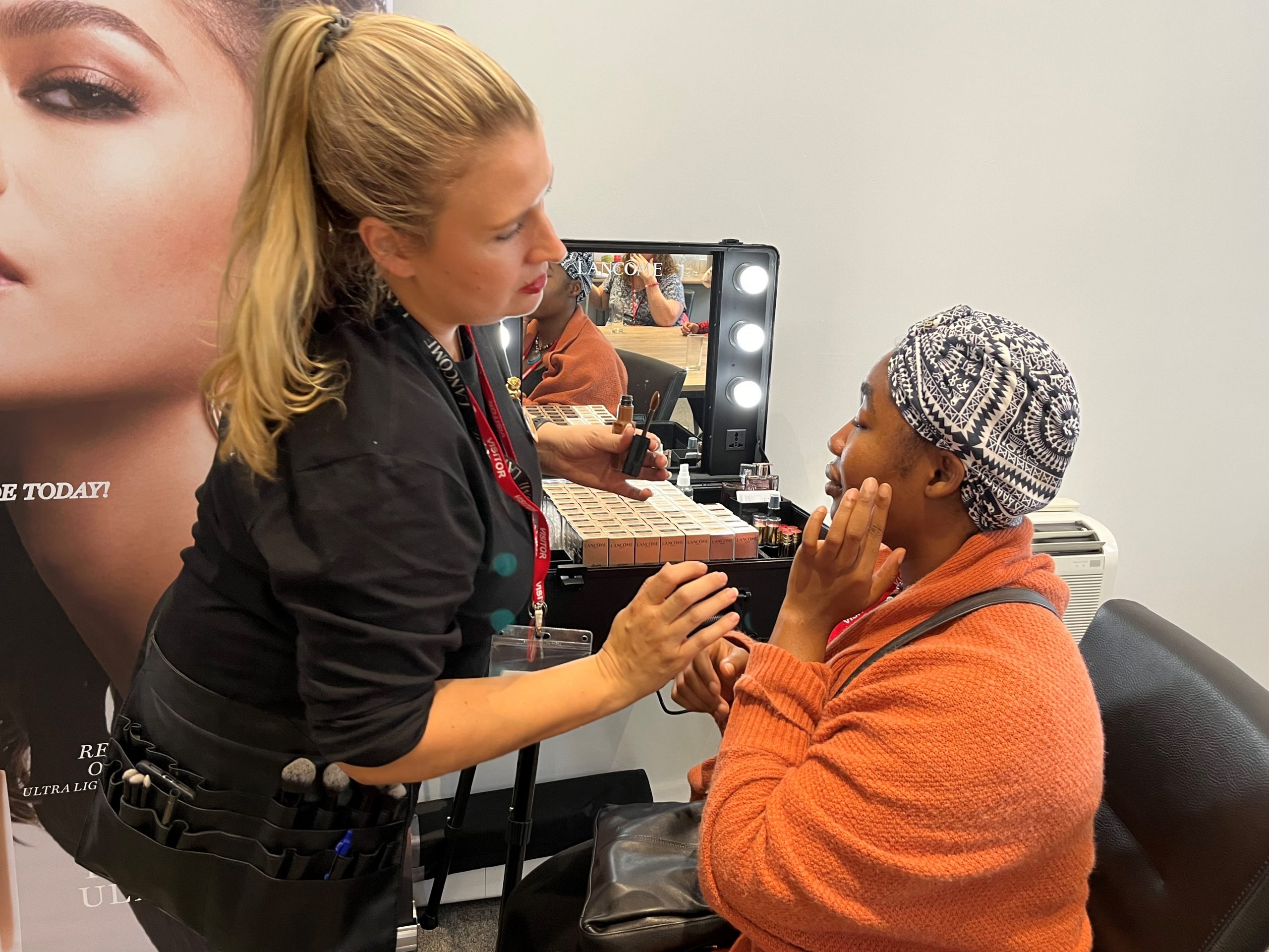 A make-up artist with Greater Manchester SLC member, Ada Eravama. Ada is applying product to her cheek with the assistance of the makeup artist.