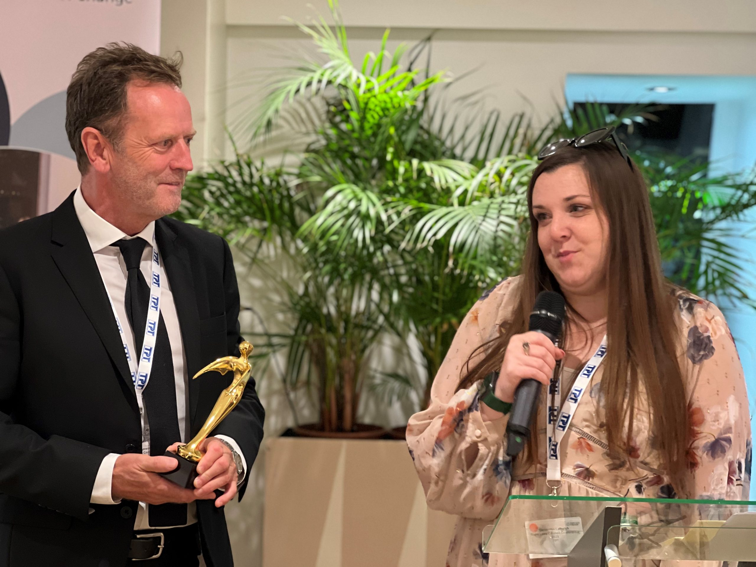 Mervyn Williamson, Trustee at TPT, pictured with Samantha Leftwich, Engagement Manager for East England. Sam is speaking into a microphone, accepting the Outstanding Contribution award on behalf of Sam Fox, Essex SLC member.