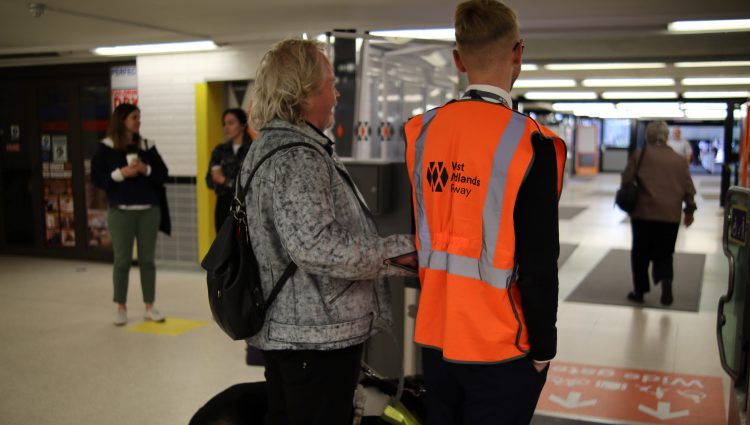 Steve Keith, Birmingham and Black Country SLC member, being guided through a ticket barrier by a member of staff. They have their backs to the camera.