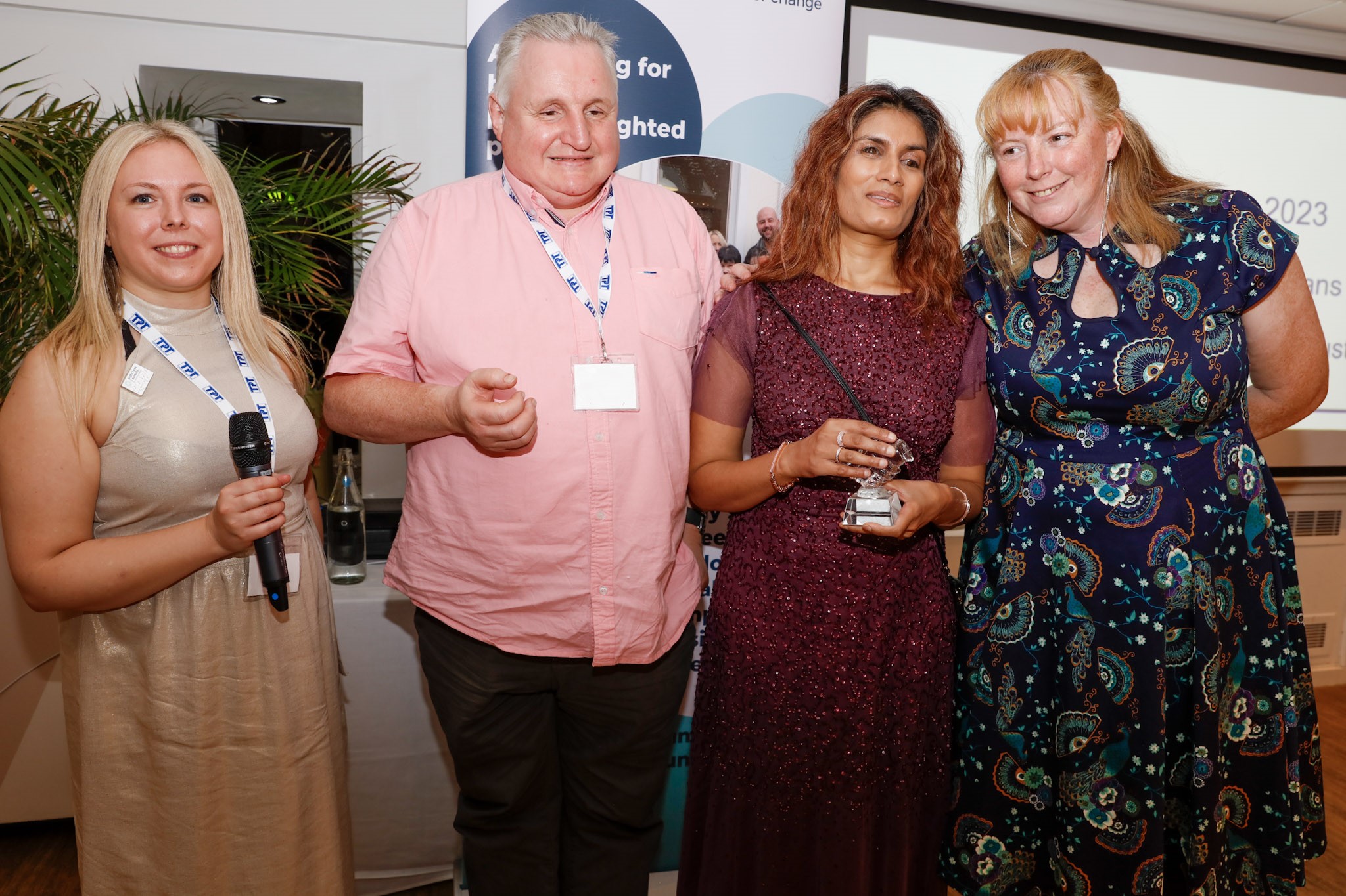 From left to right: Helen Mitchell, Trustee at TPT, Alun Davies, Anela Wood, WOE SLC member, and Tricia Sail. They are stood in a line, smiling at the camera. Anela is holding their award for Team of the Year.