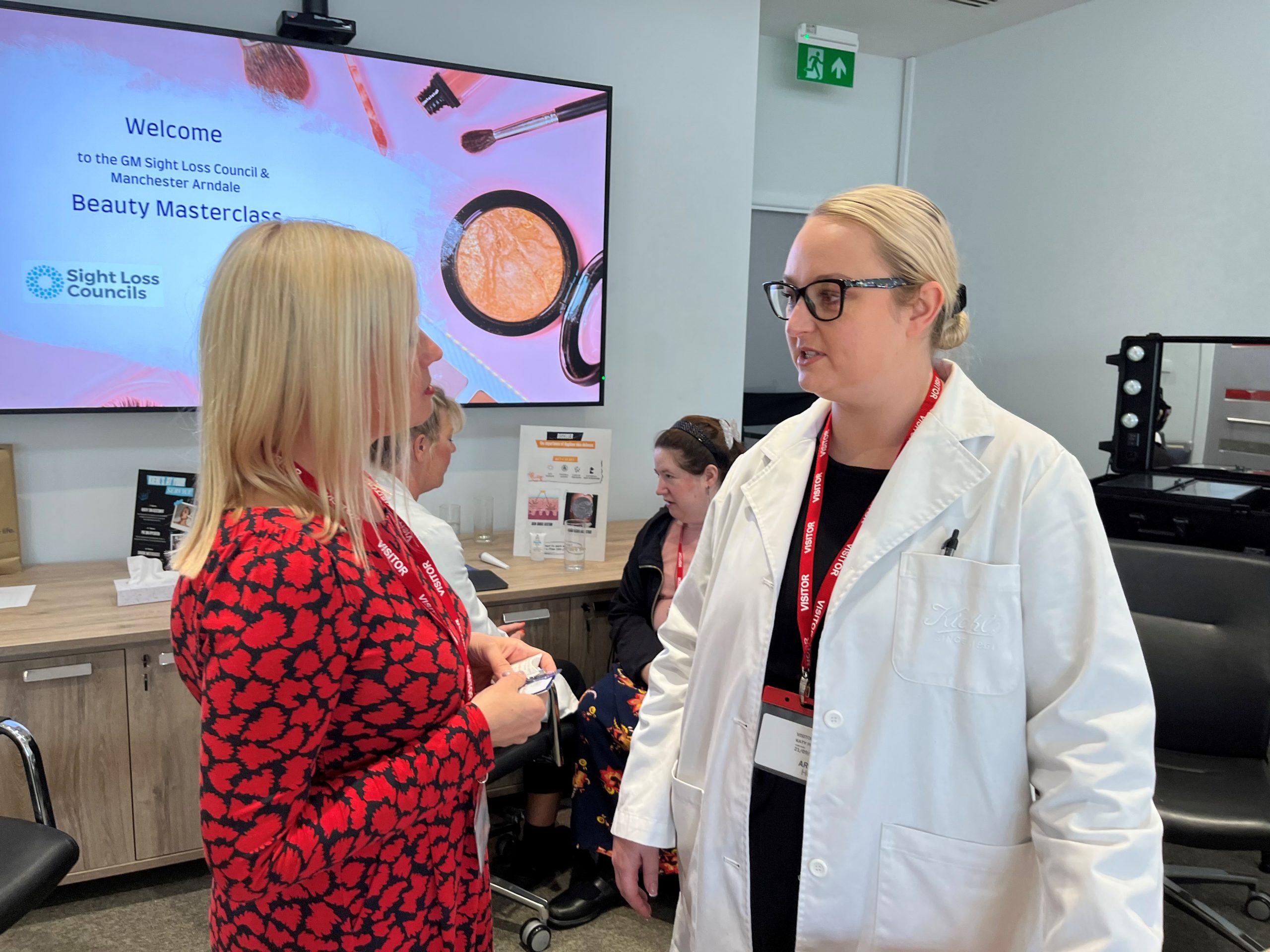 Kelly Barton, Engagement Manager for the North West, photographed talking to a Lancome representative. An attendees is shown sitting in the background during her one to one with a skincare specialist.