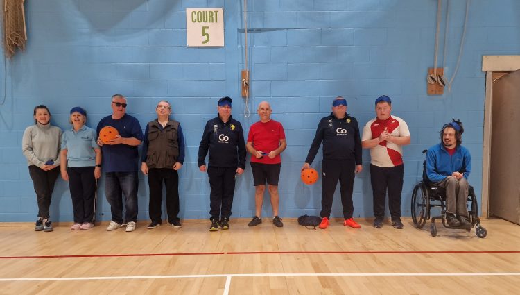 Lets Get Active attendees are standing in a line in the main sports hall, waiting for the Goalball session to start.