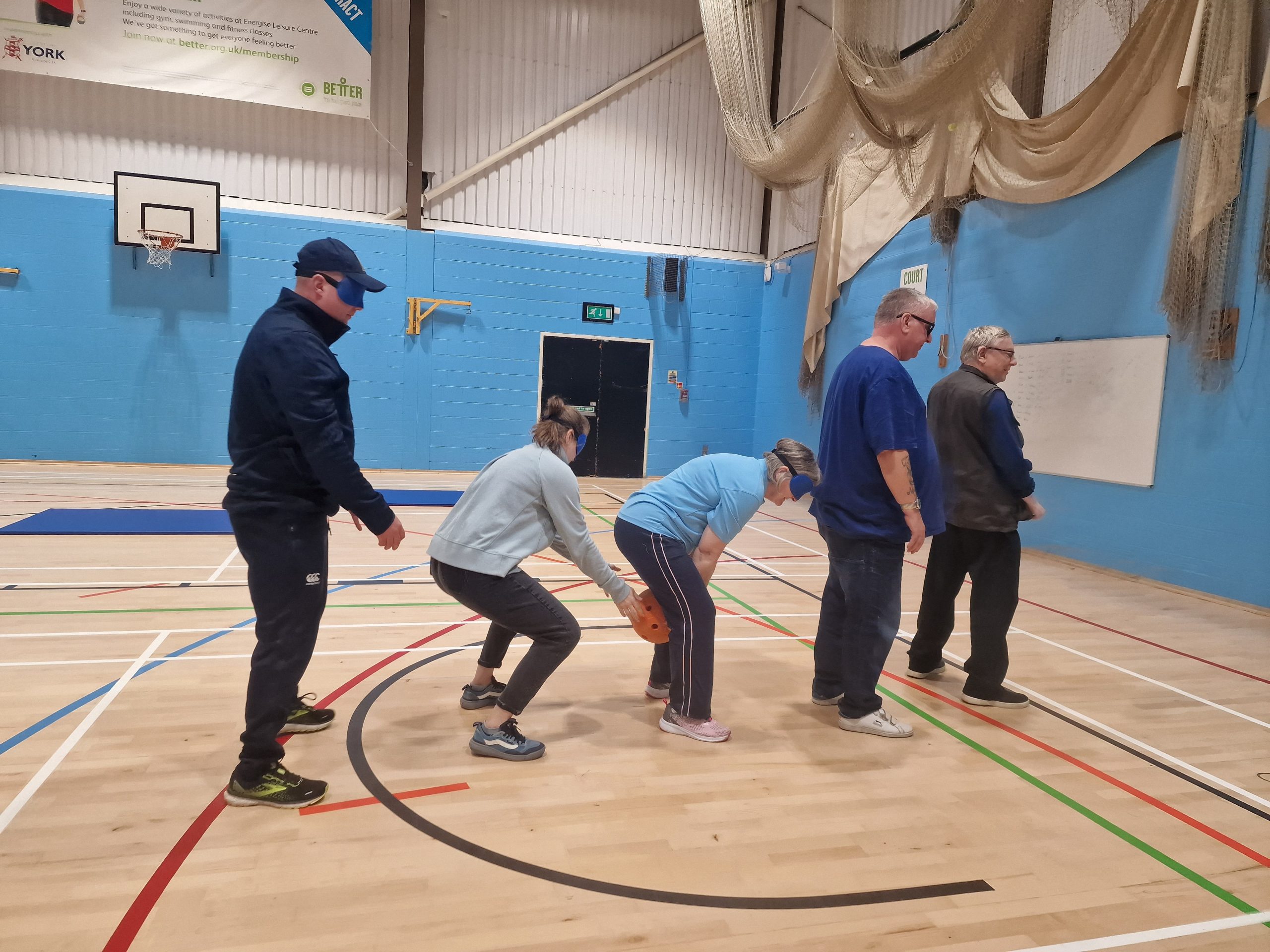 Five attendees stood in a single line during the goalball session, passing the ball to each other, through their legs,