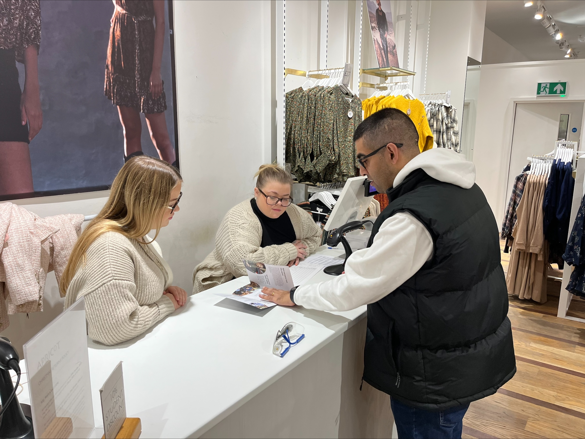 Jagdeep, Birmingham and Black Country SLC member, is standing at a counter in a clothing store, talking to two female retail assistants. He is showing them our Top Tips for Retail resource.