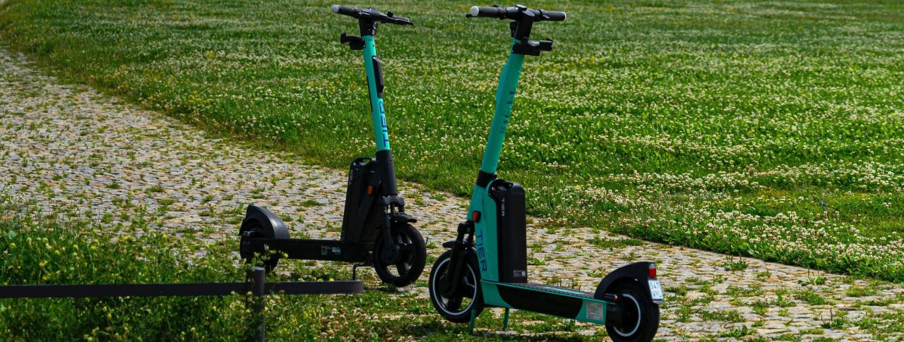 Two Tier e-scooters face each other parked on a path in the middle of a green field.