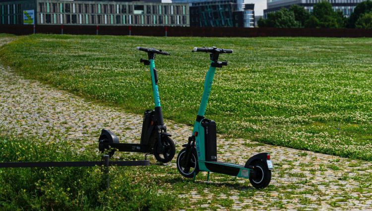 Two Tier e-scooters face each other parked on a path in the middle of a green field.