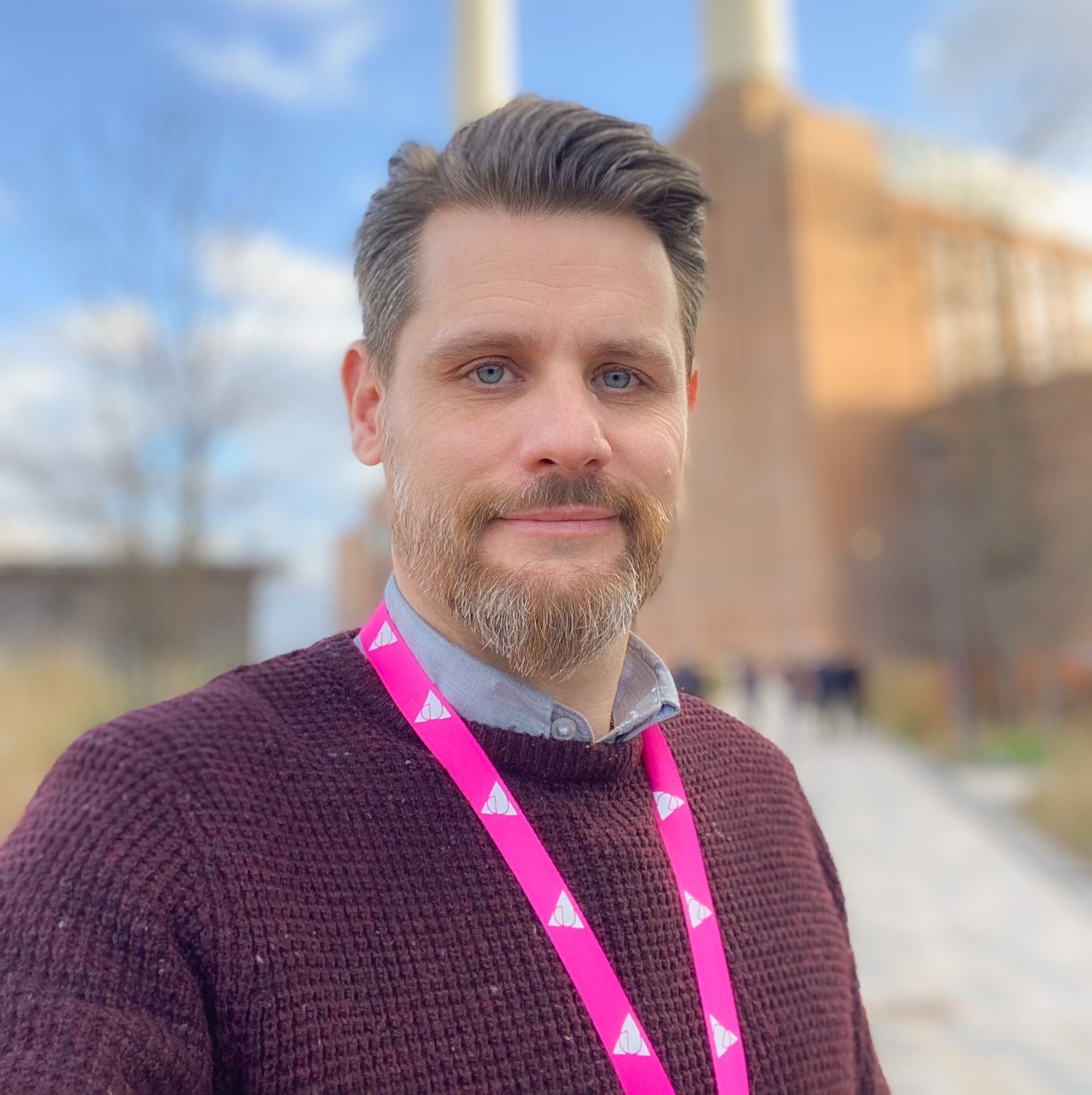 Head shot of Jean-Paul Hewlett, Head of Guest Services at Battersea Power Station. He is stood outside infront of Battersea Power Station, smiling at the camera.