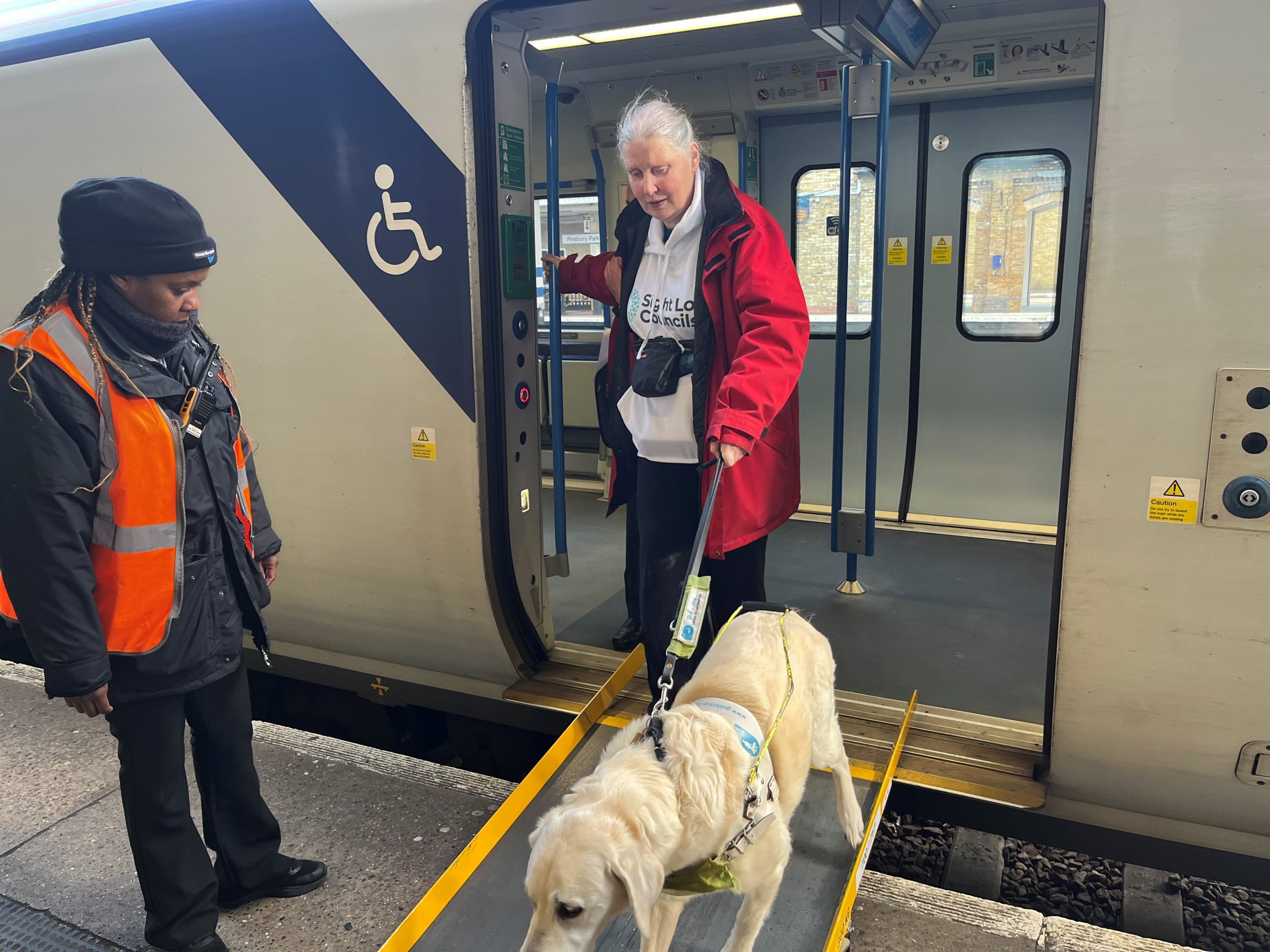 Mary Cox, South West London SLC member, disembarking a train with her guide dog, as a member of staff looks on.