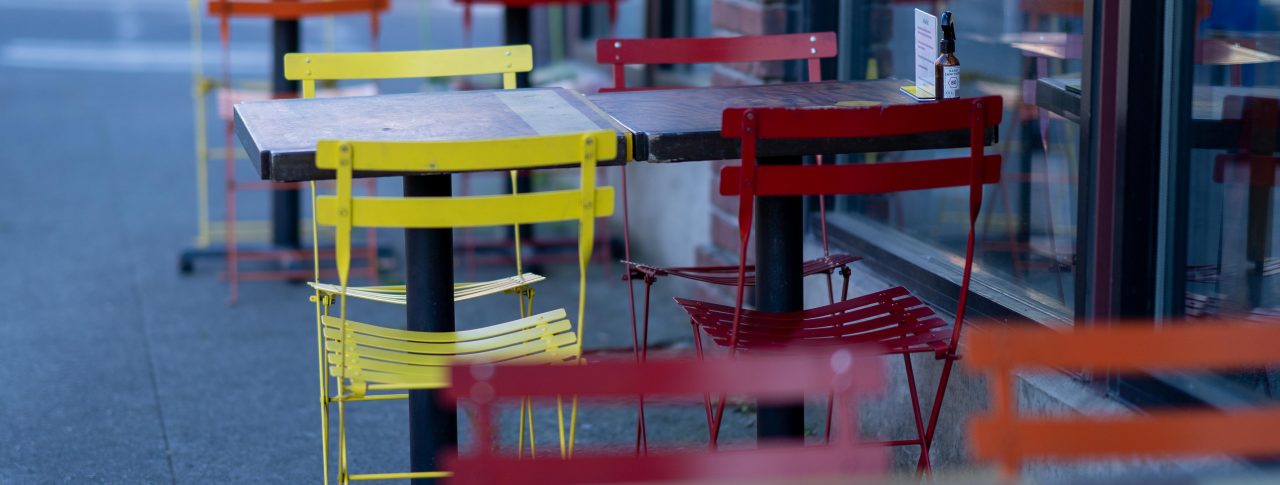 Red and yellow chairs placed on either side of a table outside a cafe.