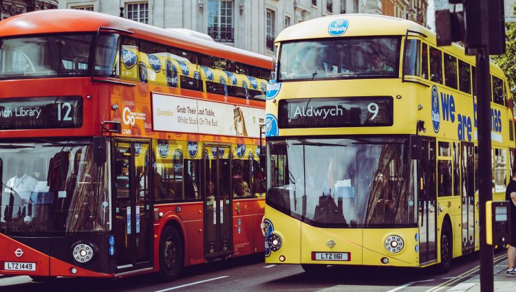 A pair of London buses driving down the road. The one of the right says Aldwych and the number 9 at the front.