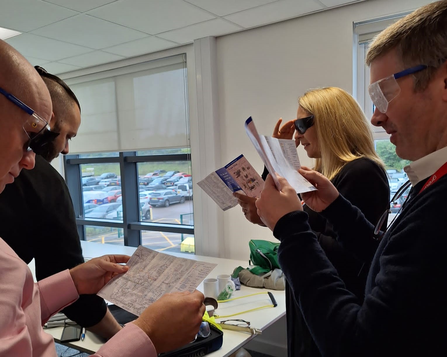 Greater Anglia staff members are stood together, wearing sim-specs, trying to read tube maps with them on.