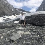Steve Holiday, Tyne and Wear SLC member, standing on a mountain, surrounded by rocks with some ice and snow shown in around him. He is wearing shorts!