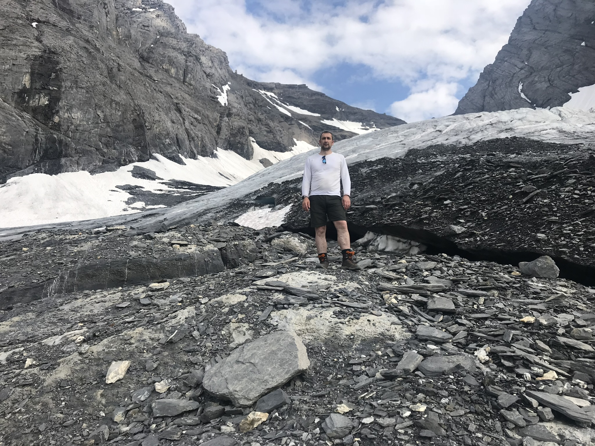 Steve Holiday, Tyne and Wear SLC member, standing on a mountain, surrounded by rocks with some ice and snow shown in around him. He is wearing shorts!