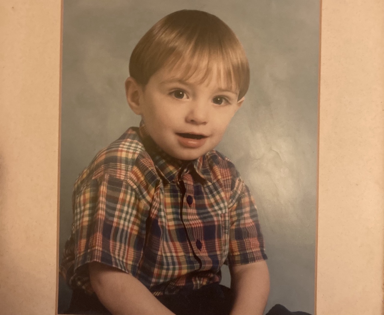 A photo of Jack, aged three years old. He is siting down, wearing a short sleeve plaid shirt. He is smiling at the camera.