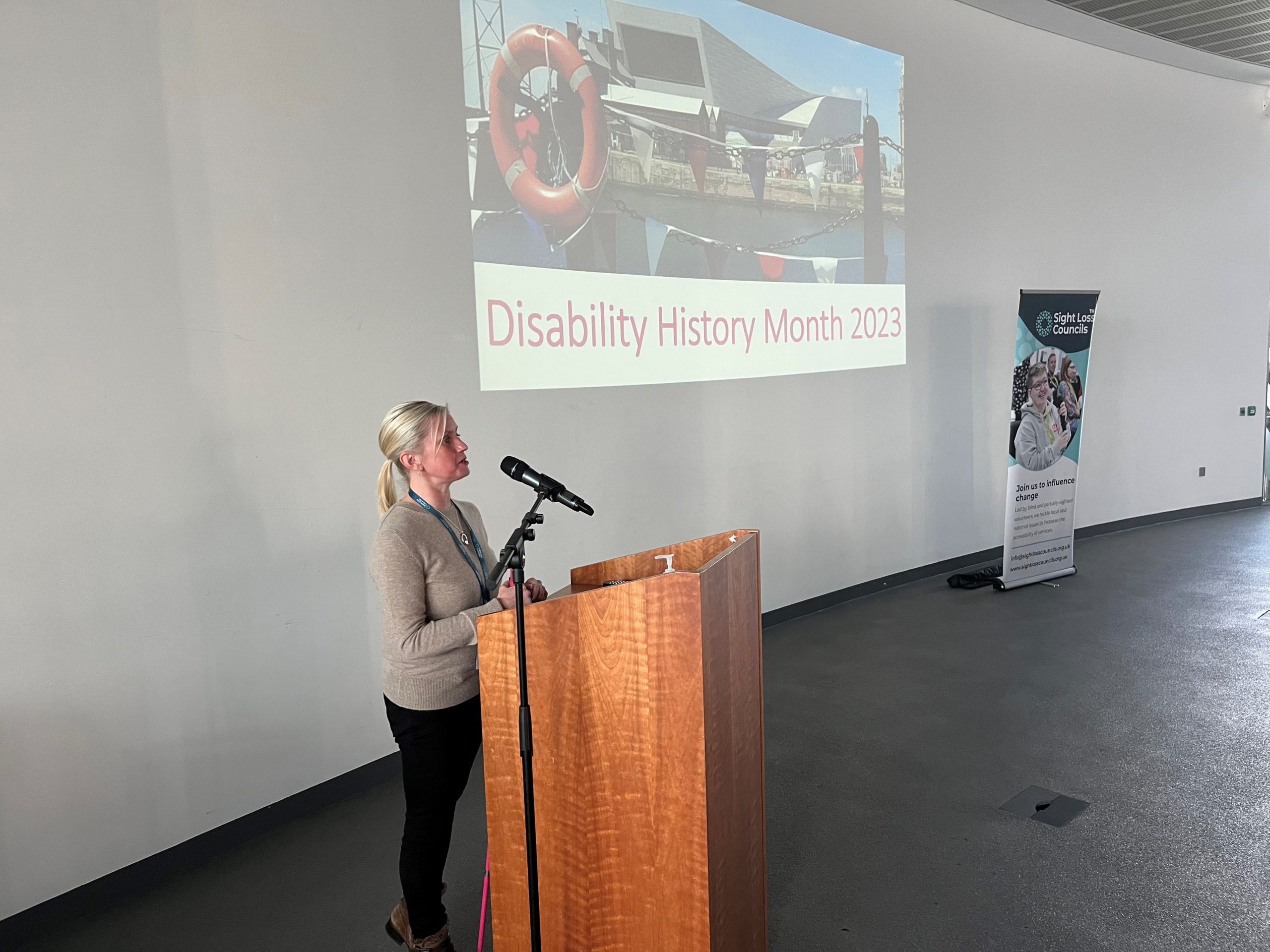 Kelly Barton, Engagement Manager for North West England, addressing delegates during the event. A presentation slide says ‘Disability Awareness Month’ 2023 and there is a Sight Loss Council banner in the background.