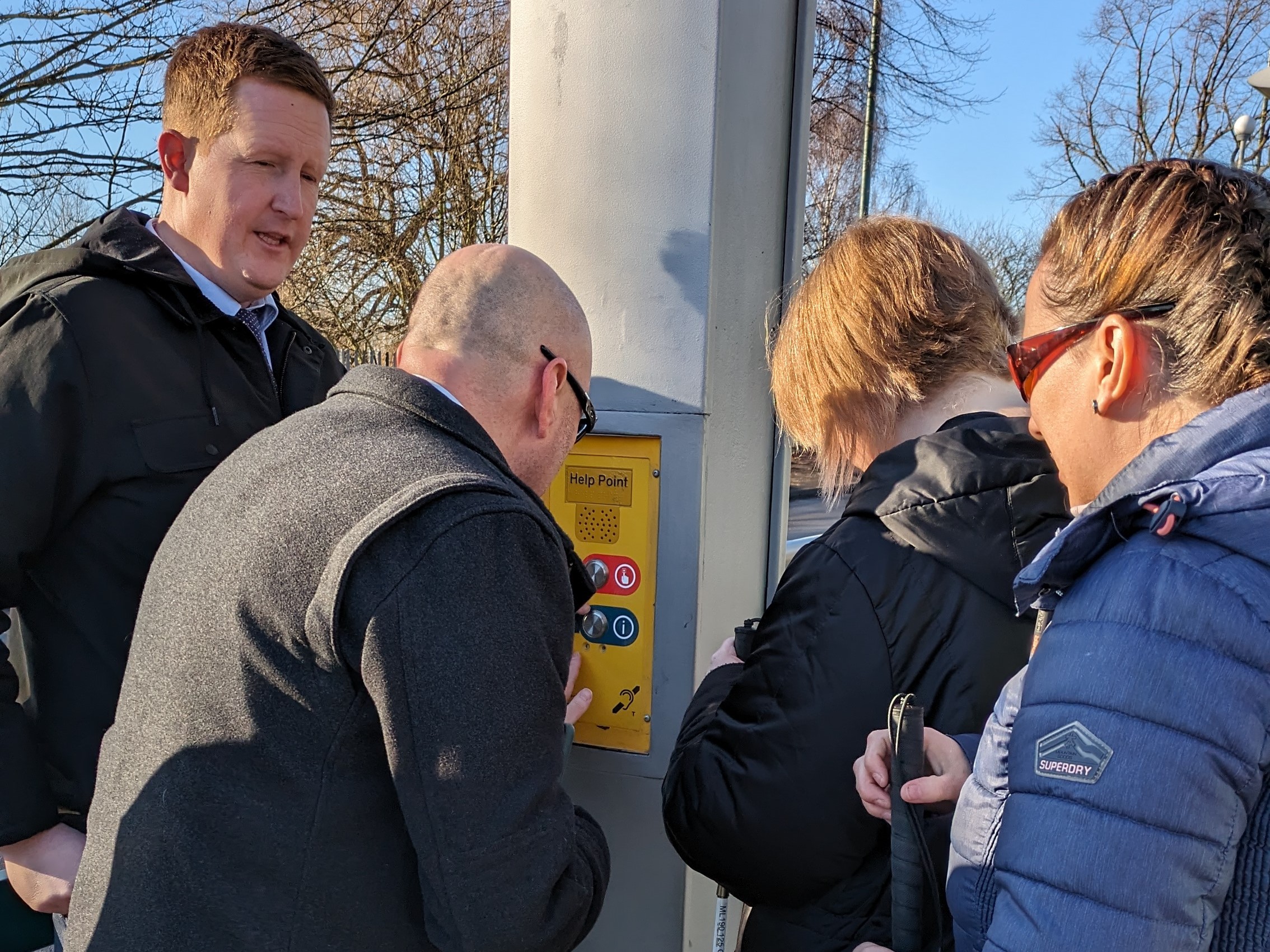 Conor from NET, Engagement Manager Matt Harrison, and SLC members Kay and Sian, stood around a help point as Conor talks them through its use.