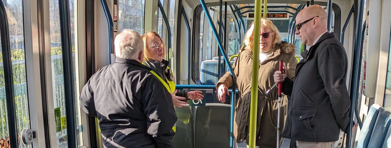 Notts SLC members stood on a tram with a representative from NET. They are stood together talking.