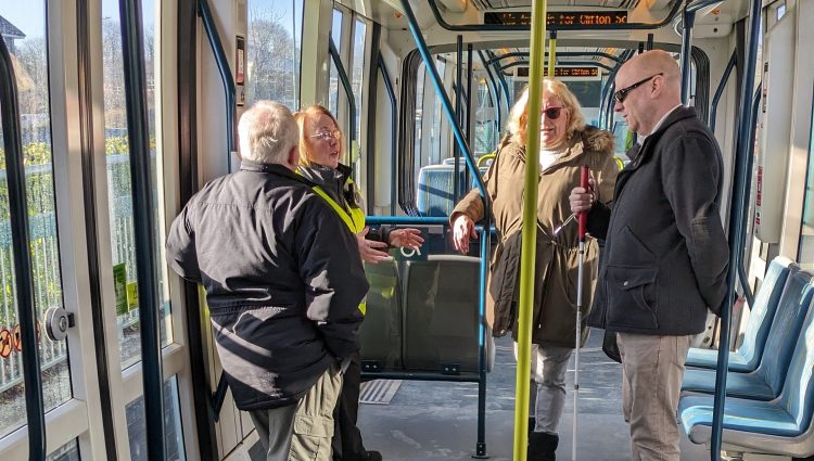 Notts SLC members stood on a tram with a representative from NET. They are stood together talking.