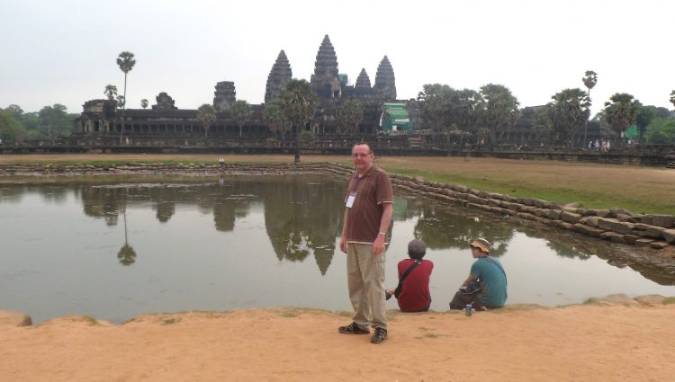 Michael Parkinson, Lancashire SLC member, stood at Angkor Wat in Cambodia. Michael is standing by a stretch of water, with Angkor Wat in the distance.