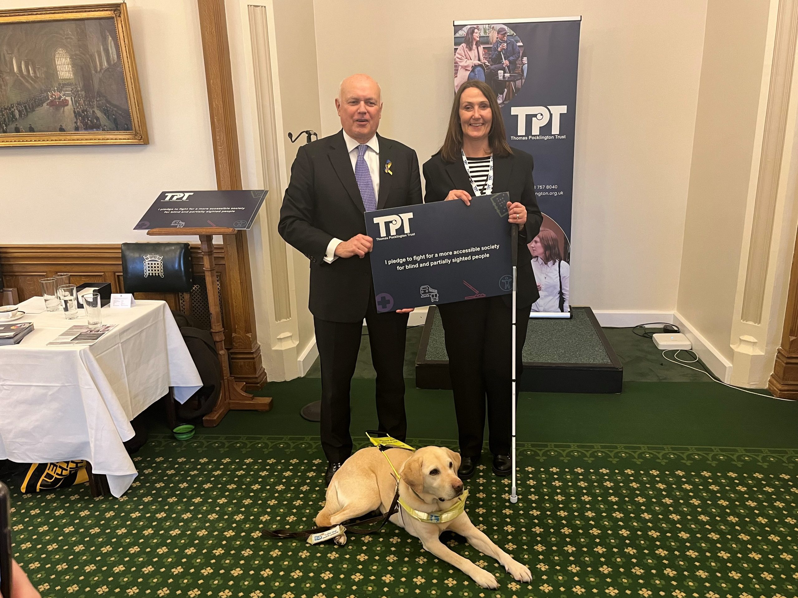 Iain Duncan Smith, Conservative MP for Chingford and Woodford Green, pictured with Cathy Low, Director of Partnerships at TPT holding the TPT pledge. Guide dog Anna is laying on the floor in front of them.