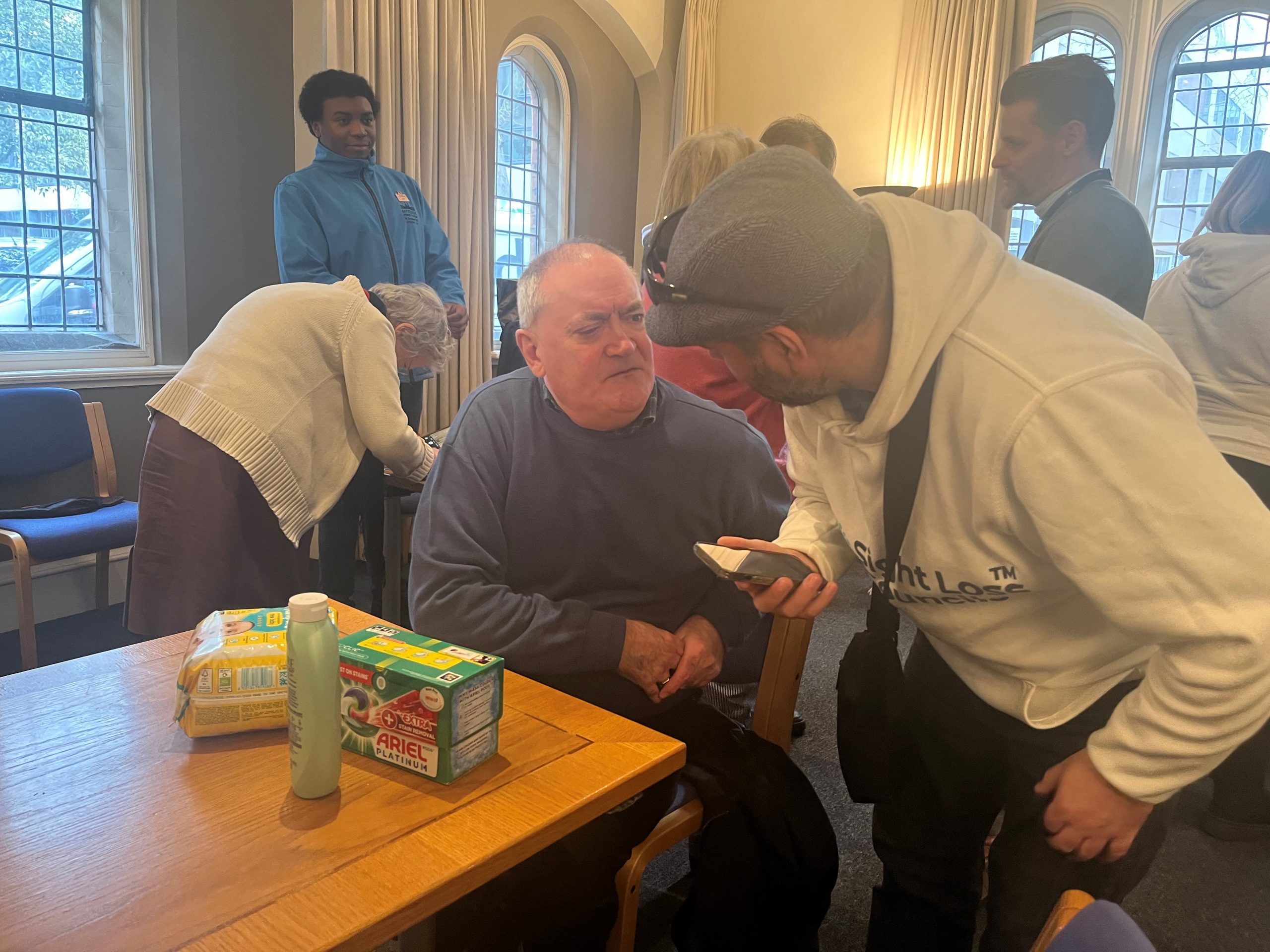 SLC member, Steve Reed, pictured holding his smart phone, and talking to a delegate who is looking up at him. On the table in front of them are three products which have the NaviLens code on them.