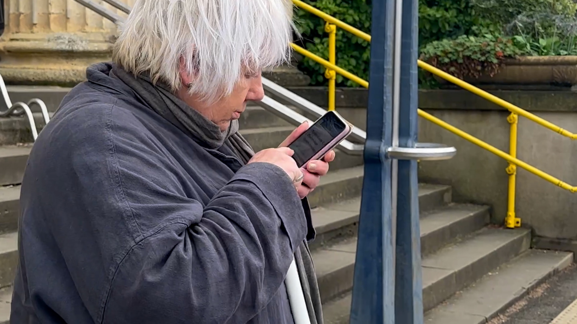 Ann Lightfoot, SLC member, looking at her smartphone, accessing the audio guides, outside the hospital.
