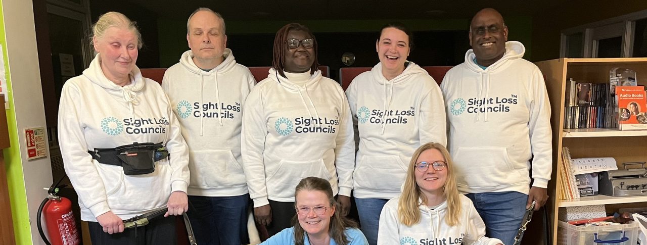 Sight Loss Council volunteers and staff pictured at their first anniversary. They are smiling at the camera and wearing Sight Loss Council hoodies.