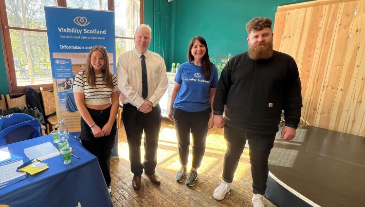 Photo taken at the launch event of Sight Loss Councils Scotland. From left to right: Lara, SLC volunteer, Iain Mitchell, Senior Engagement Manager for Sight Loss Councils North, Emma Scott, Head of Operations, Visibility Scotland, and Callum Lancashire, Engagement Manager for Sight Loss Councils Scotland. They are stood together next to a Visibility Scotland banner, smiling at the camera.