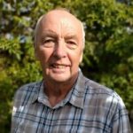 Headshot of Derbyshire SLC member, Bill. He is standing in a garden with trees behind him. He is wearing a checked shirt and smiling at tha camera.
