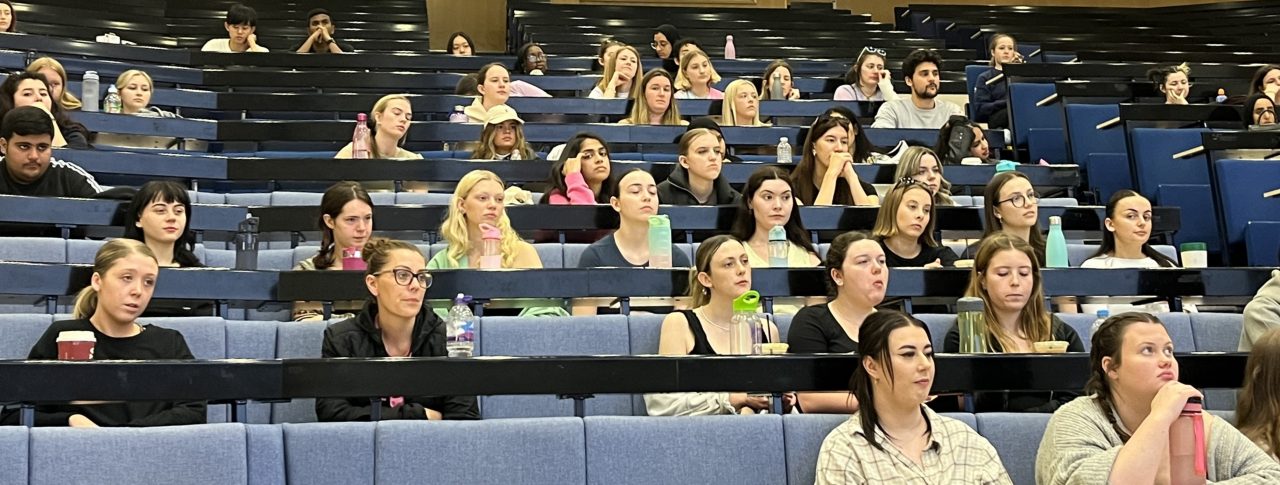 Several rows of Liverpool University healthcare students, sat in the auditorium, looking forwards to the stage.